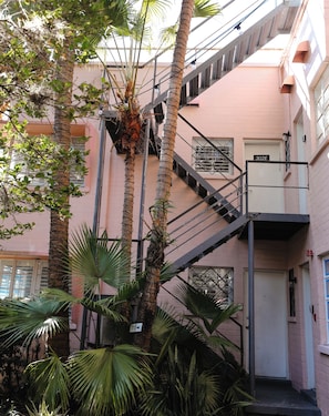 Un edificio de varios pisos con una escalera metálica, palmeras y fachada de ladrillo rosa.