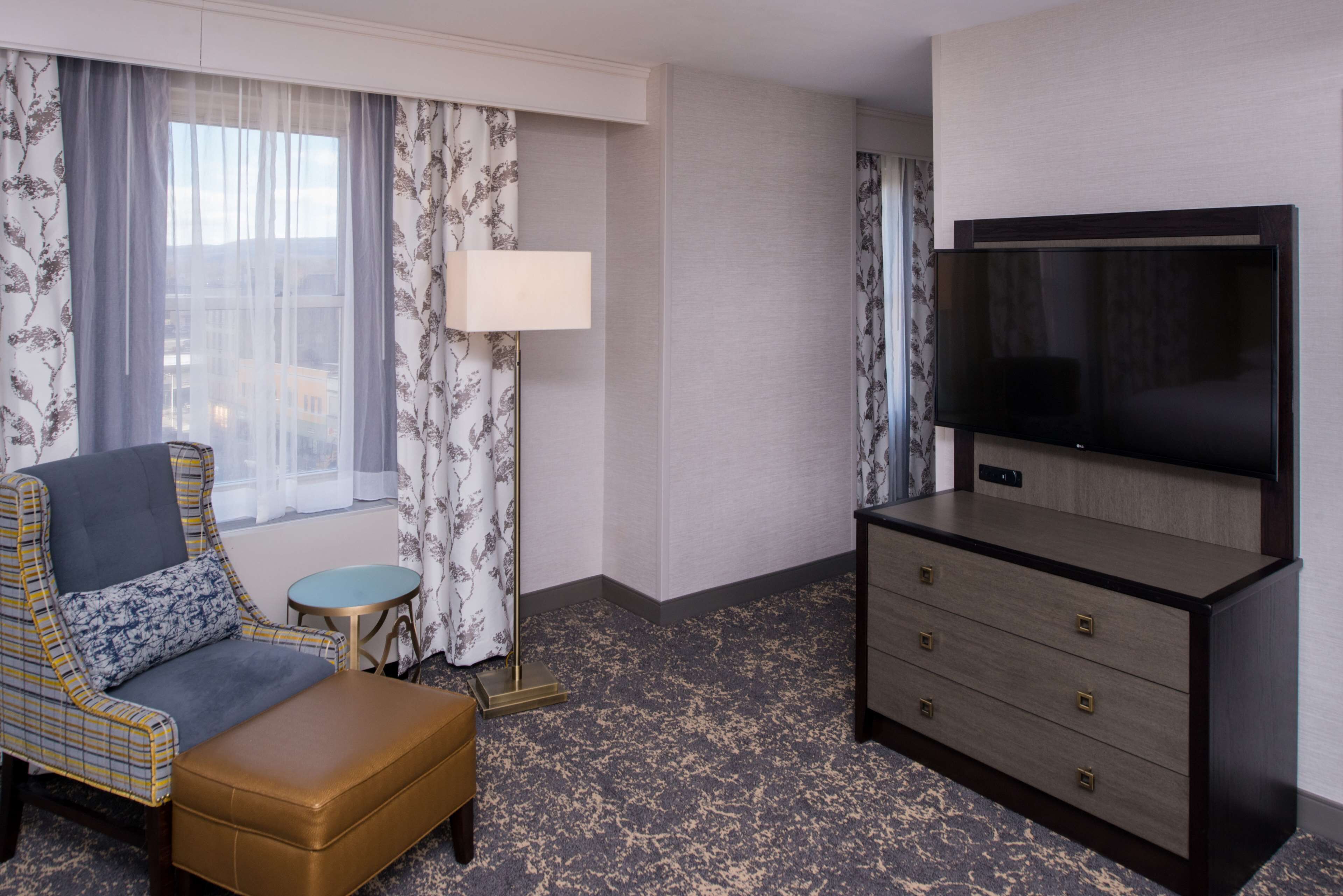 A hotel room with a large flat-screen TV, a sofa, a small round table, and a dresser.