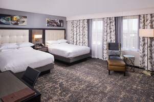 A hotel room with two beds, a desk, a chair, and a small table.