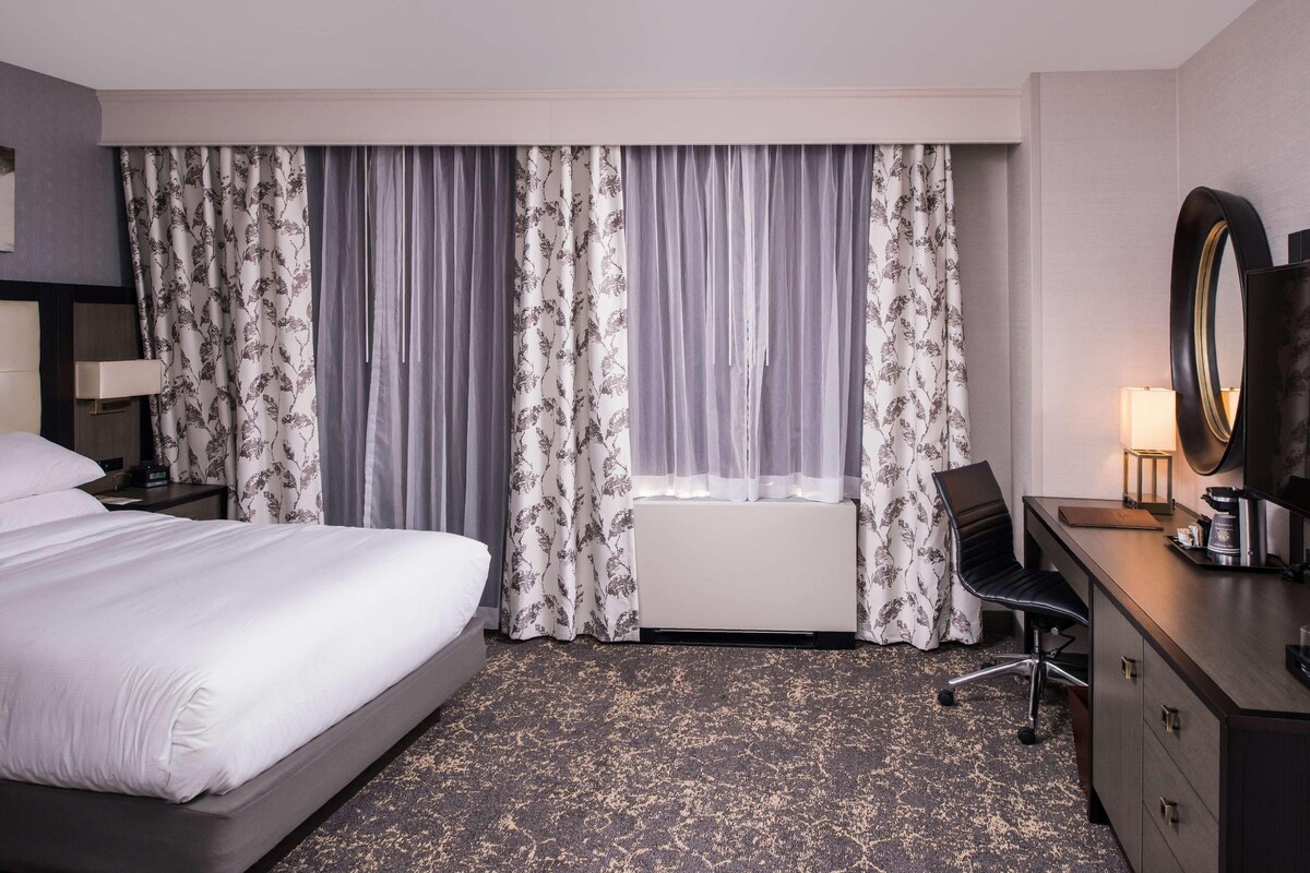 Ein Hotelzimmer mit Bett, Schreibtisch, Stuhl, großem Spiegel und Vorhängen.