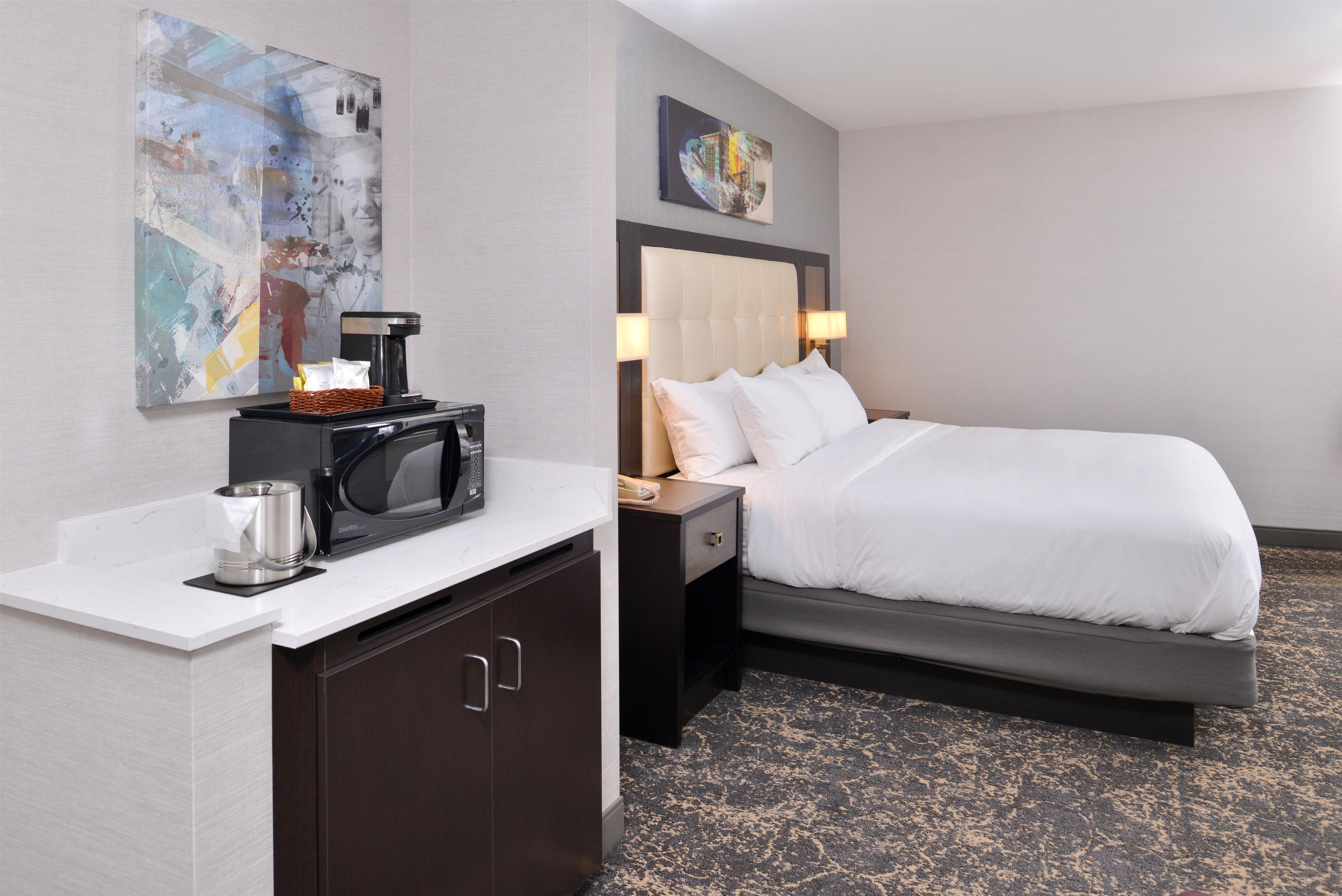 A hotel room with a bed, a bedside table with a lamp, a microwave, and a coffee maker.
