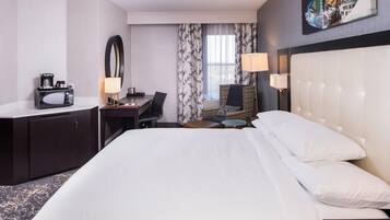 A hotel room with a bed, a desk with a computer, a chair, a small table, a lamp, and a coffee maker.