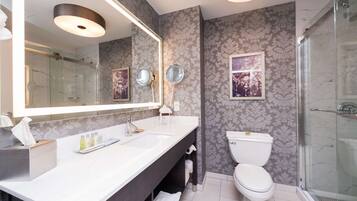 A modern bathroom with a large mirror, dual sinks, a toilet, and a glass-enclosed shower.