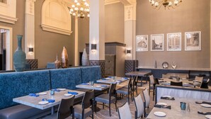 A restaurant with blue cushioned booths, rectangular tables, and modern chandeliers. - DoubleTree by Hilton Utica (Utica)