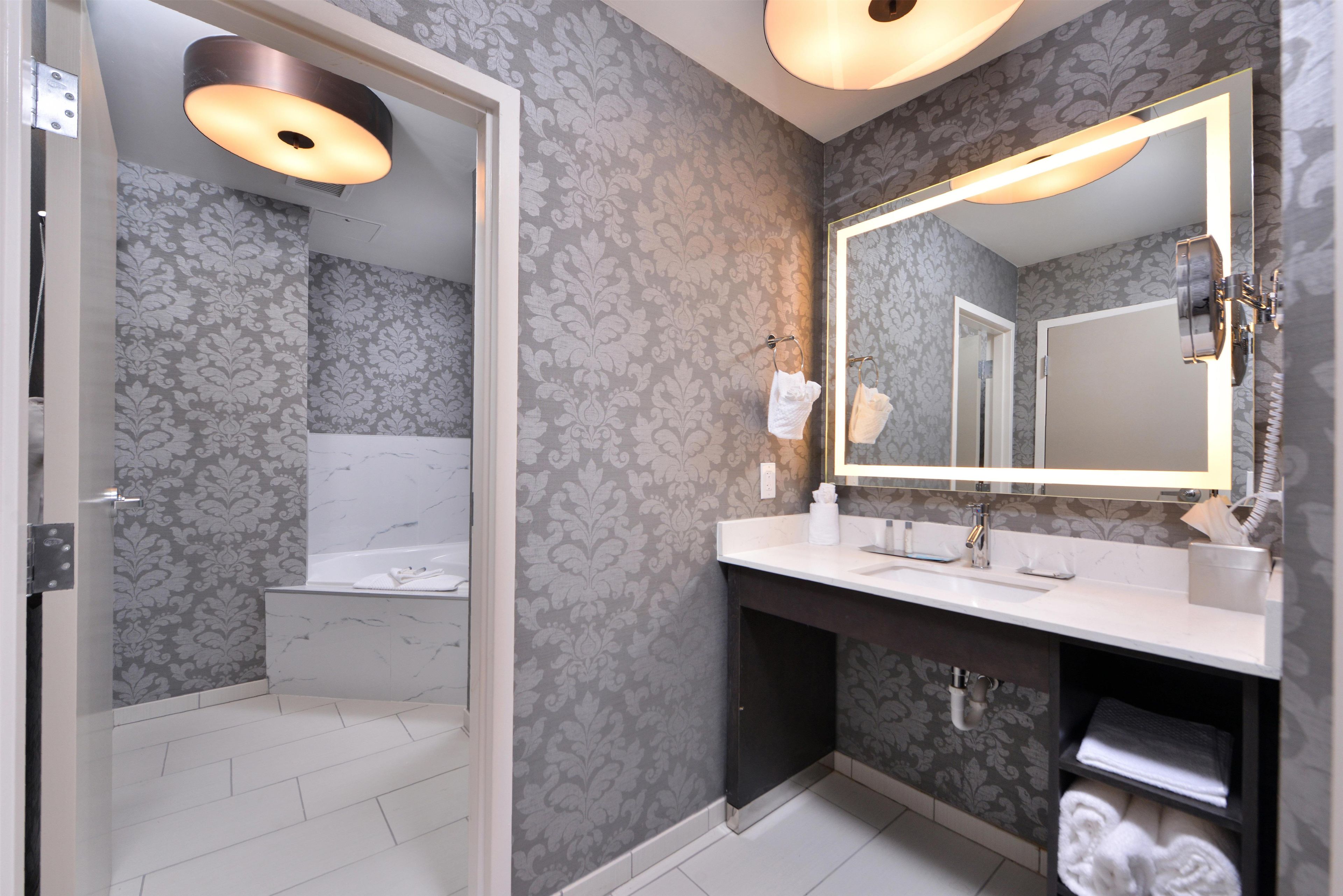 A modern bathroom with a large mirror, a bathtub, and a vanity with a sink.
