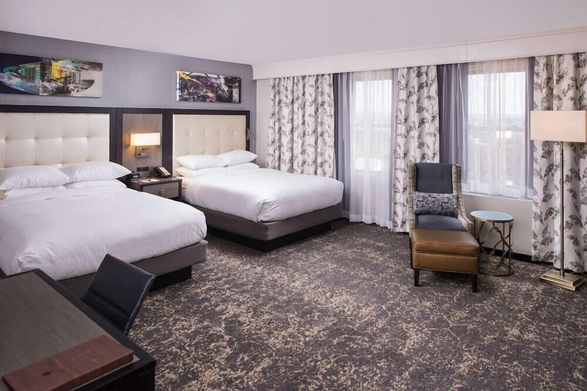 Ein Hotelzimmer mit zwei Betten, einem Schreibtisch, einem Stuhl und einem kleinen Tisch.