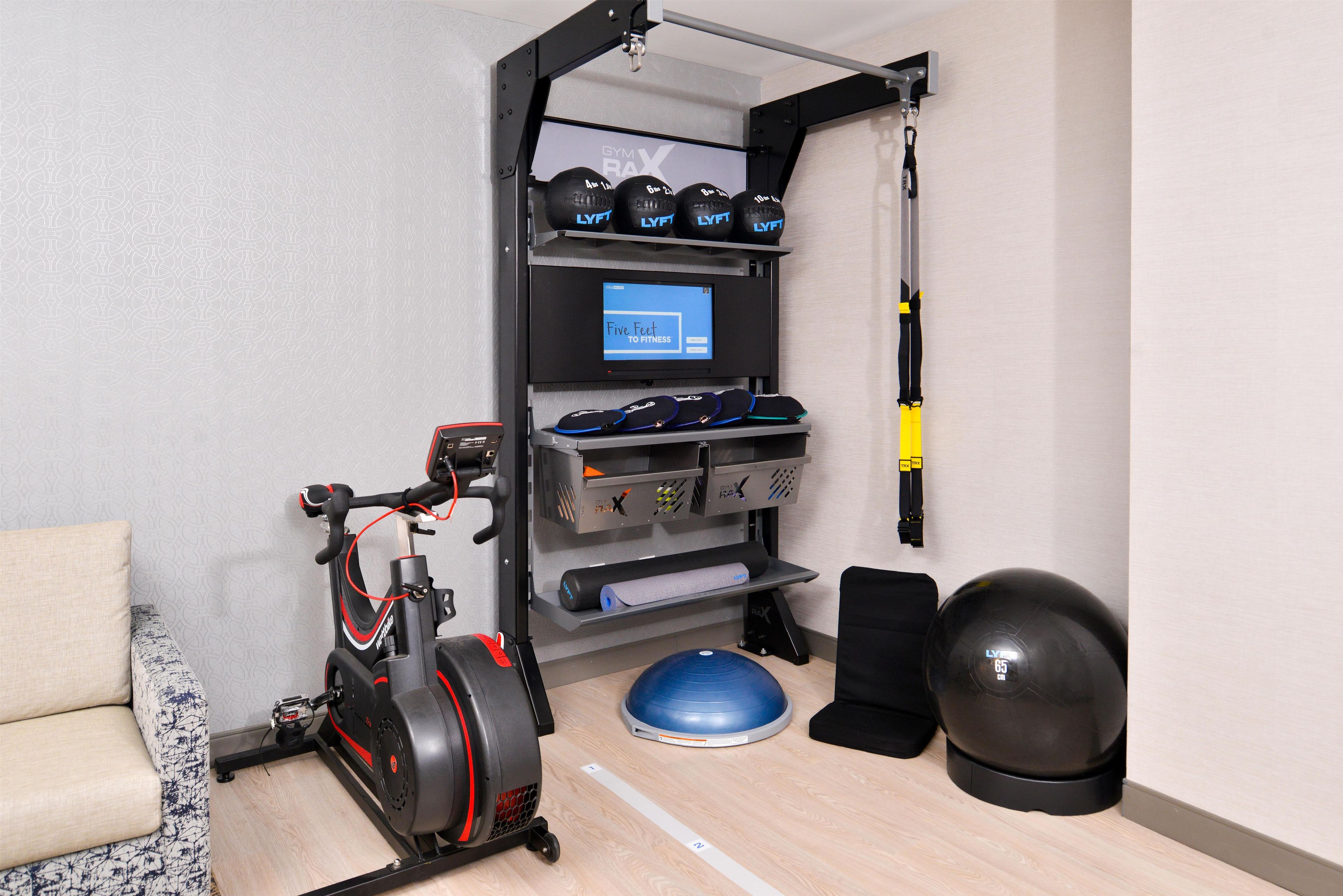 Gimnasio en casa equipado con una bicicleta estática, discos de pesas, un saco de boxeo y una pantalla digital.