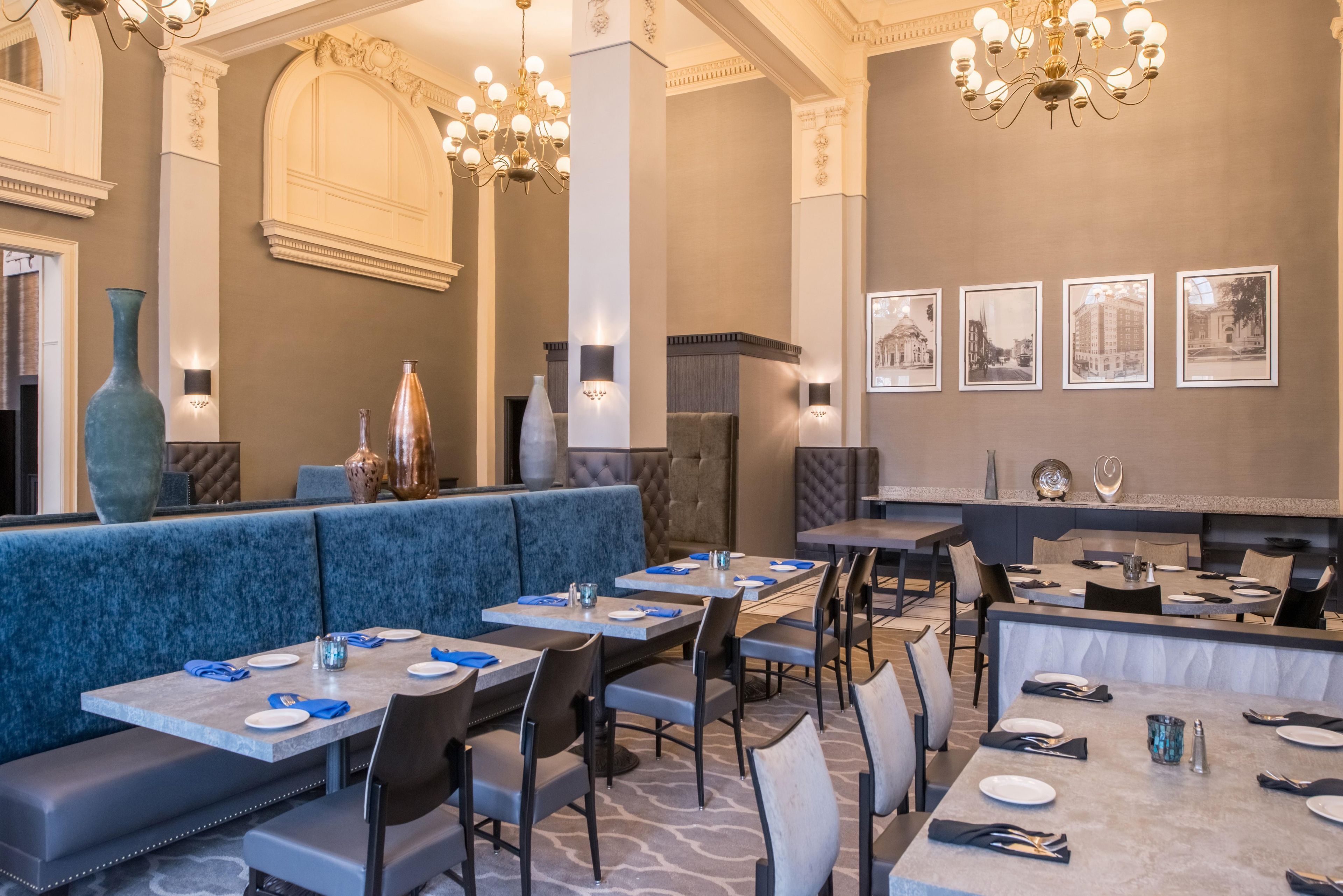 A restaurant with high ceilings, chandeliers, and a long counter with tables and chairs.