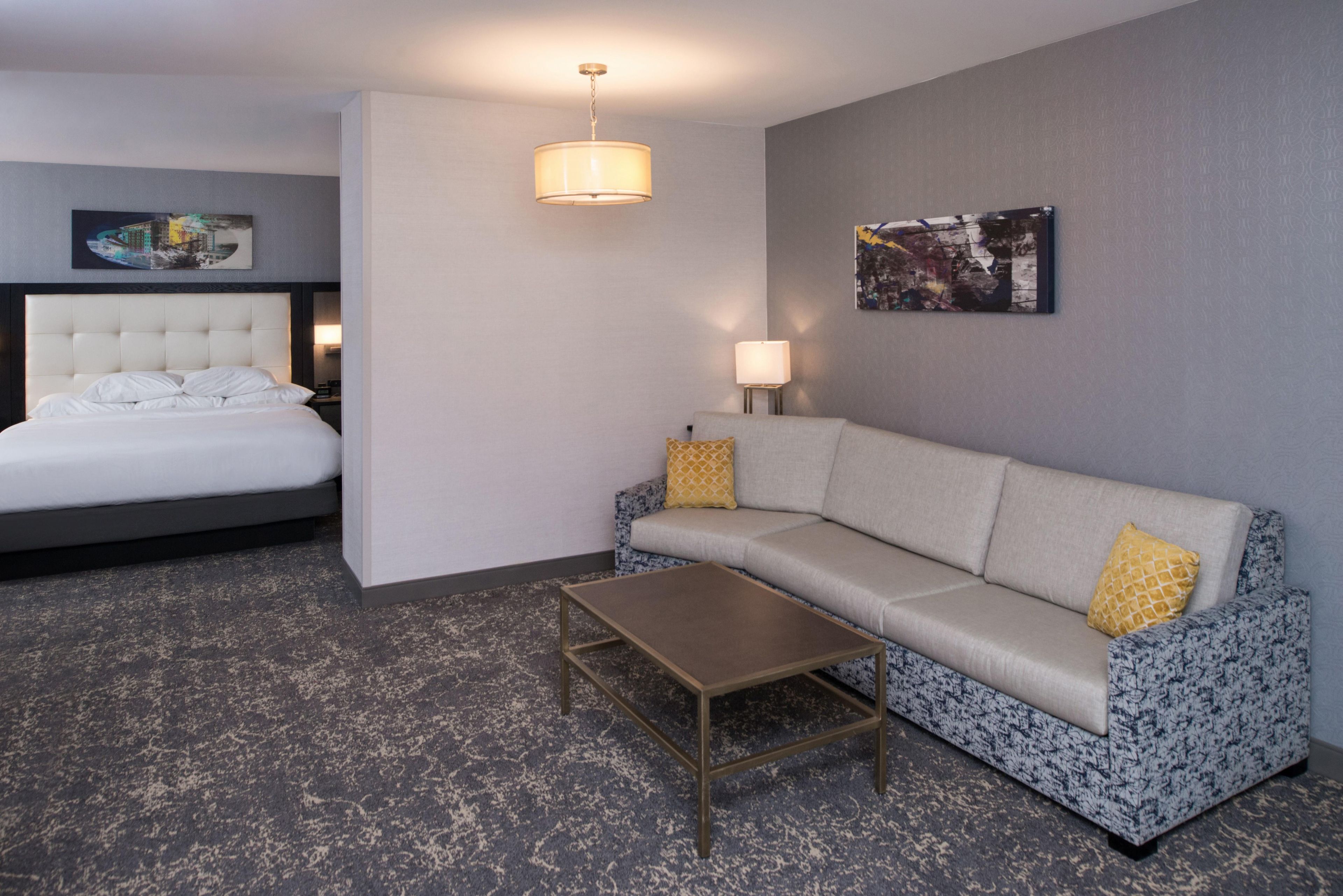 Habitación de hotel con cama, sofá, mesa de centro, lámpara y dos obras de arte en la pared.