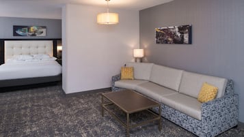 Habitación de hotel con cama, sofá, mesa de centro, lámpara y dos obras de arte en la pared.