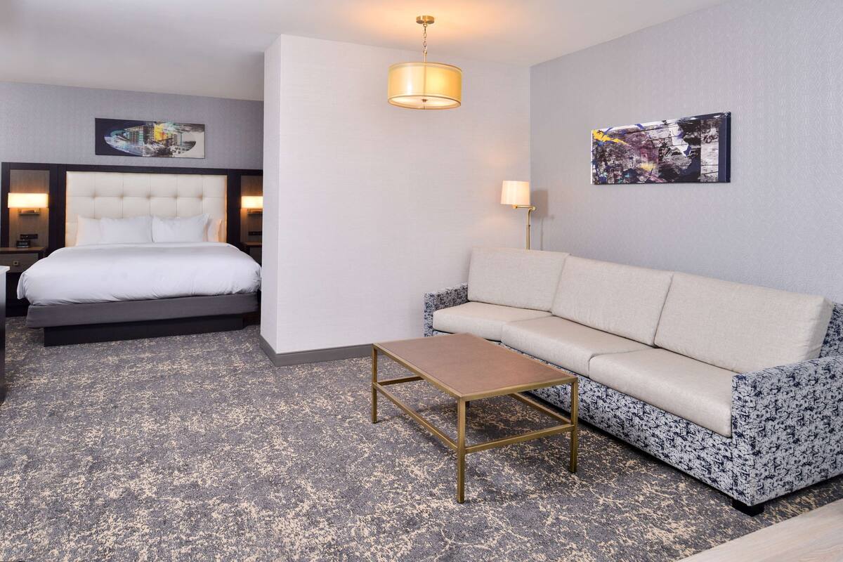 A hotel room with a bed, a sofa, a coffee table, and two wall-mounted lamps.