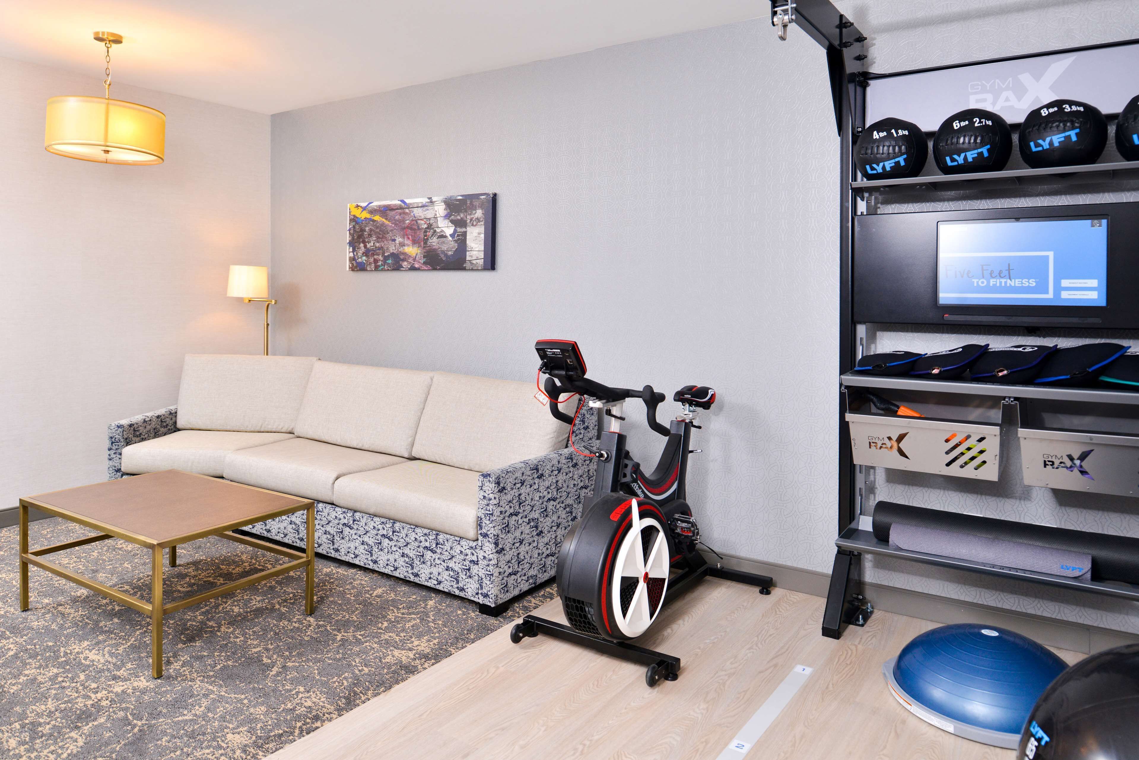 A living room with a sofa, a coffee table, an exercise bike, and a rack with exercise equipment.