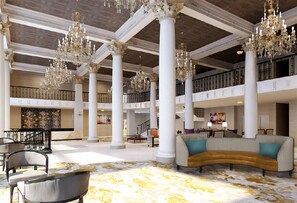 Un vestíbulo amplio con techos altos, candelabros ornamentales y una zona de estar central con un sofá curvo.
