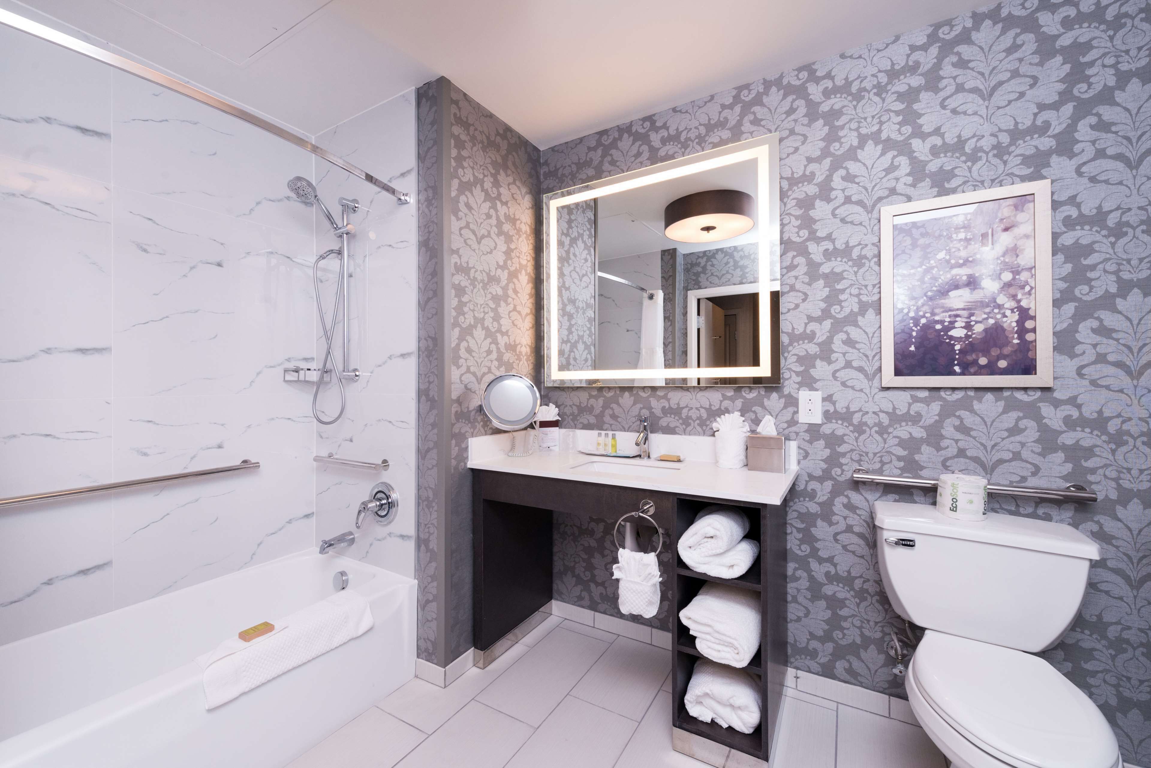 A modern bathroom with a bathtub, toilet, vanity, and a large mirror.