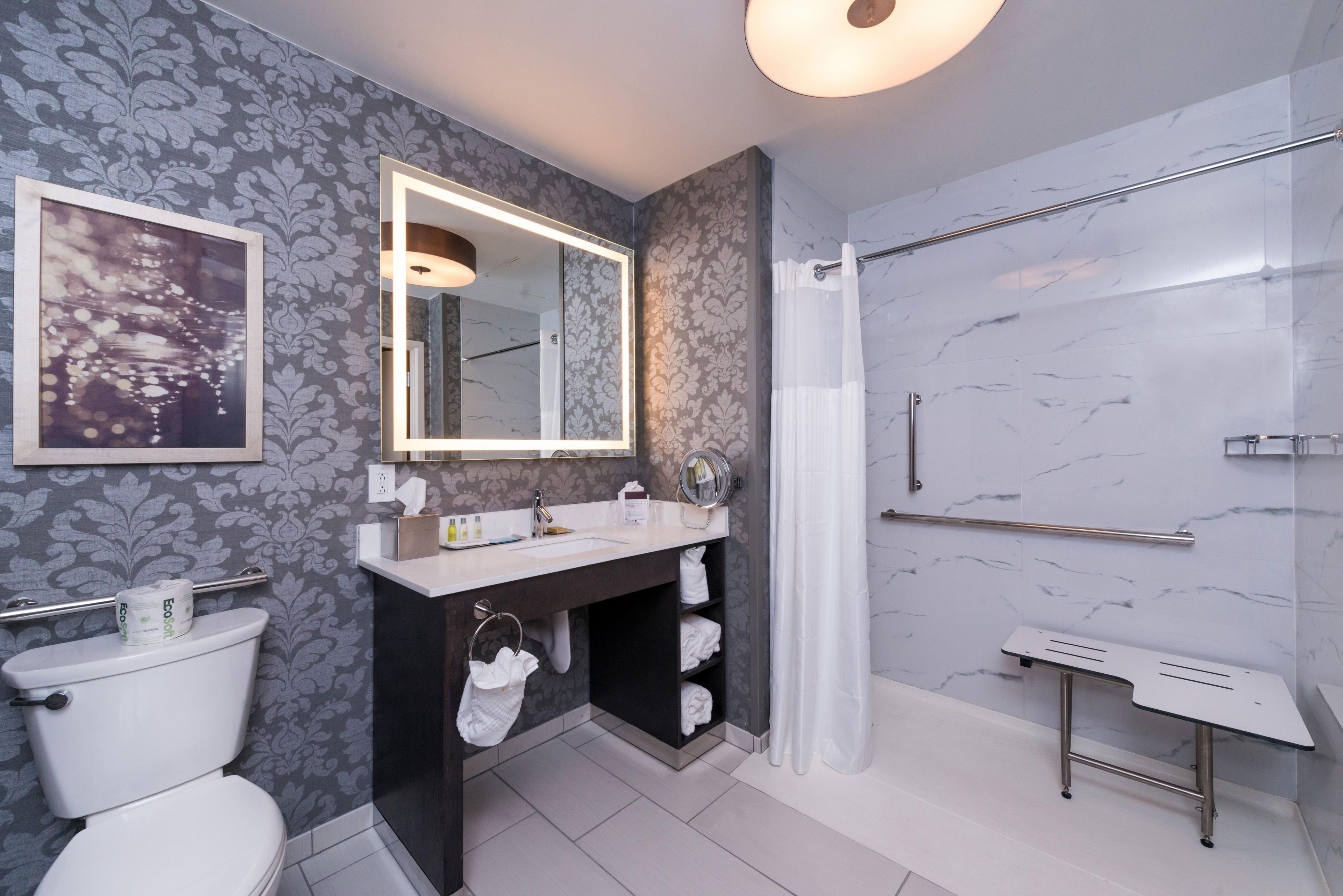 A modern bathroom with a toilet, vanity, mirror, shower, and a towel rack.