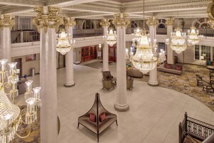 A grand lobby with multiple chandeliers, a piano, and a seating area.