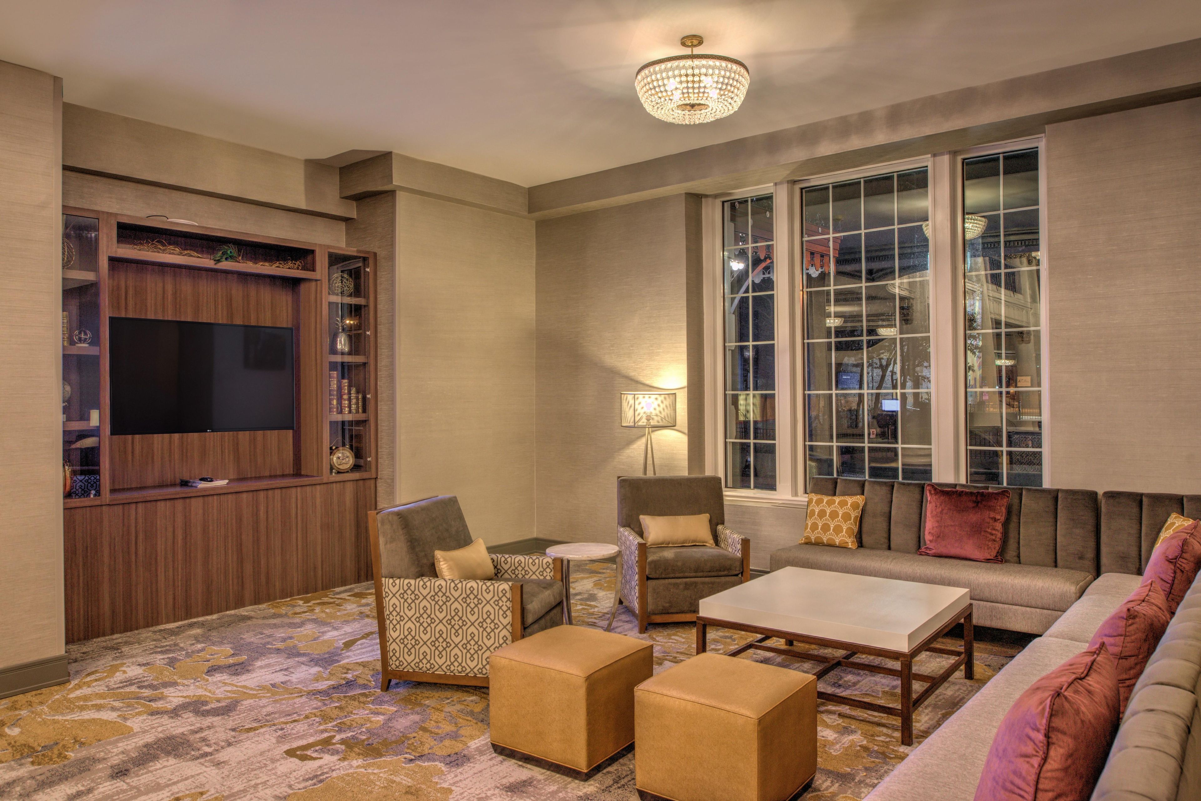 A modern living room with a flat-screen TV, a chandelier, a sofa, armchairs, and a patterned rug.