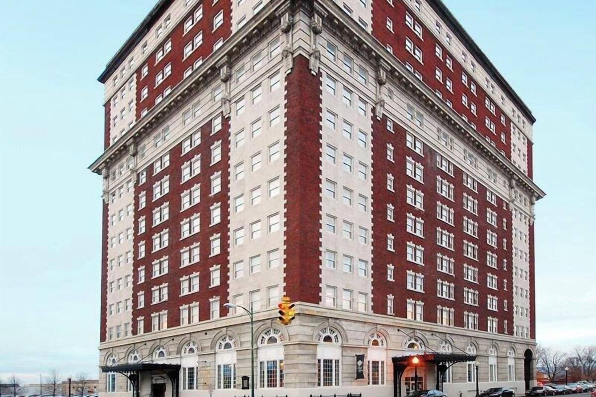 A large, multi-story building with a symmetrical facade, featuring a central entrance with arched windows and a covered area at the ground level.
