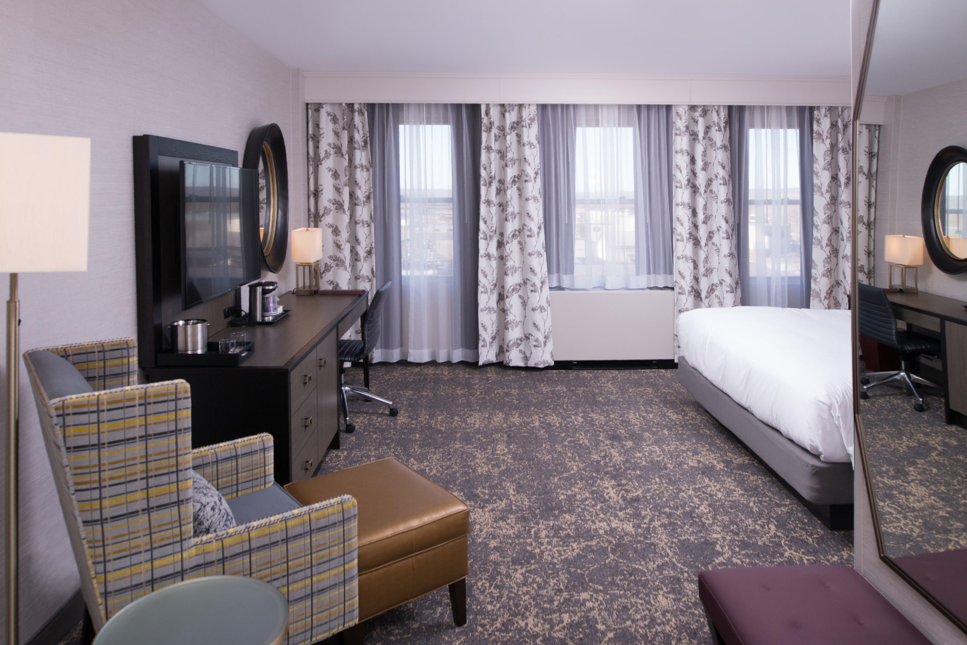 A hotel room with a bed, a desk with a chair, a sofa, and a small table with a lamp.