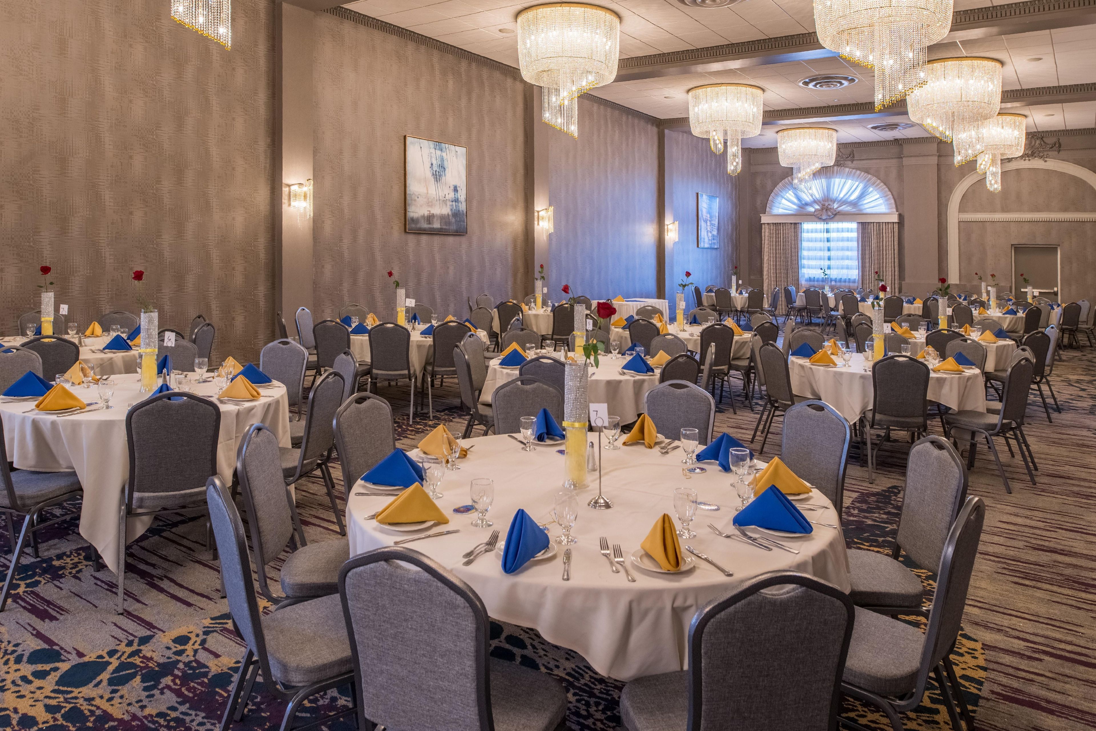 A banquet hall with round tables, grey chairs, and chandeliers.