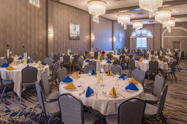 Un salón de banquetes con mesas redondas, sillas grises y candelabros.