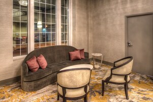 A corner room with a gray sofa, two armchairs, a small round table, and a large window with reflections.
