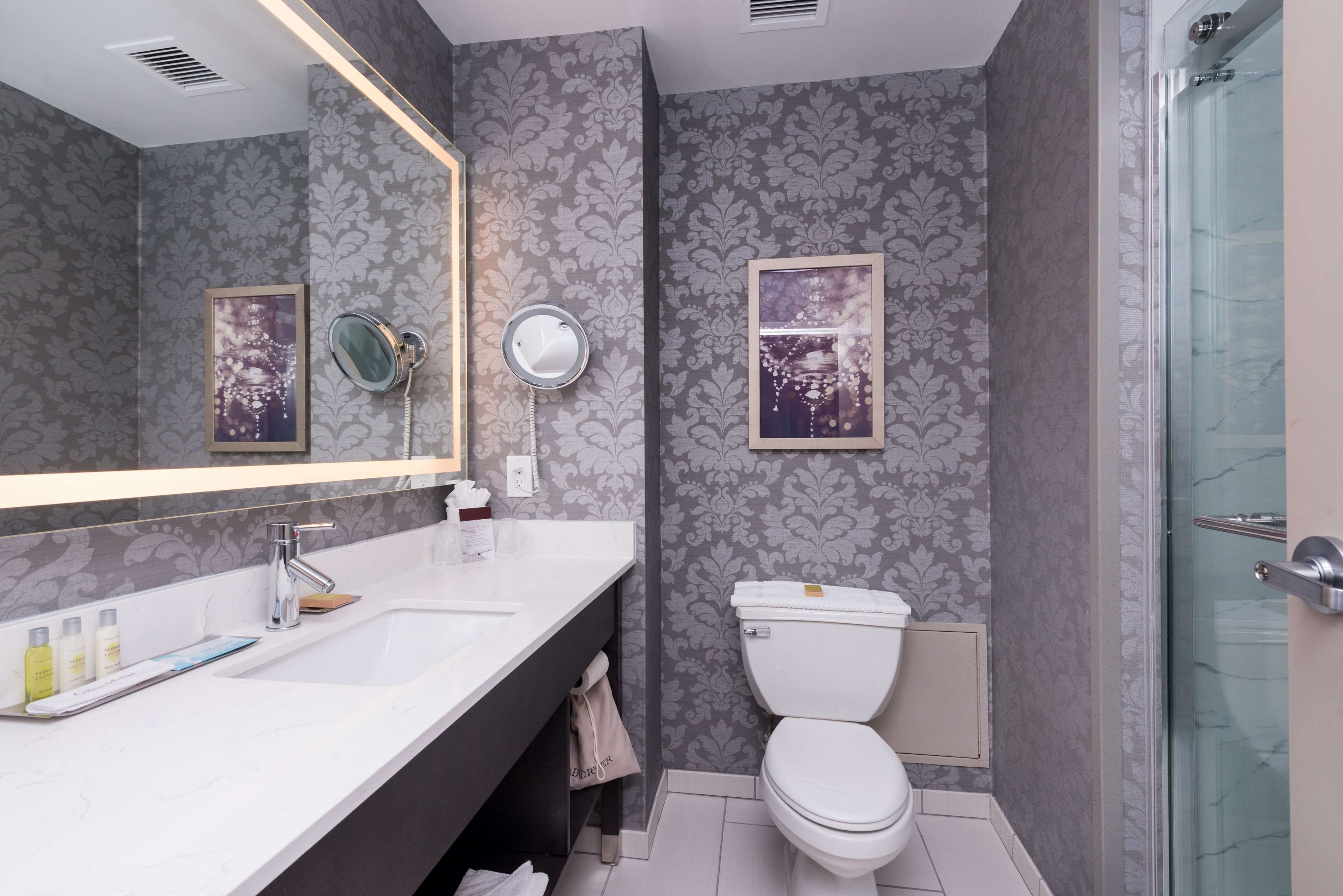 A modern bathroom with a large mirror, white sink, and a glass shower enclosure.