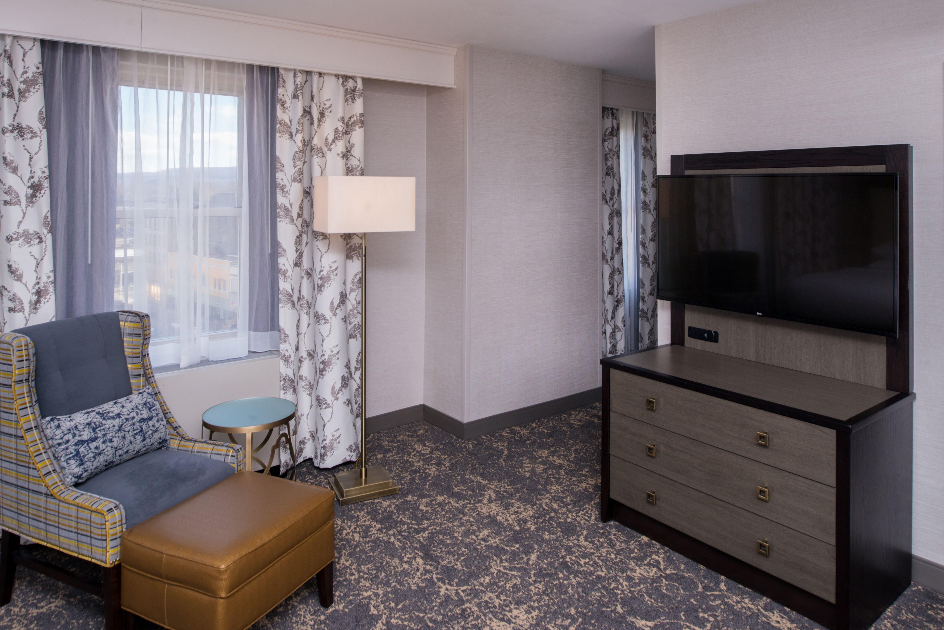 A hotel room with a sofa, a small round table, a lamp, a TV, and a dresser.
