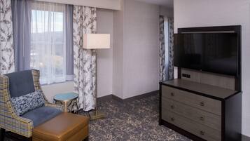 A hotel room with a sofa, a small round table, a lamp, a TV, and a dresser.