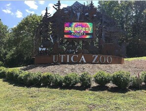 Letrero del zoológico de Utica con una exhibición colorida y la fecha de un evento.