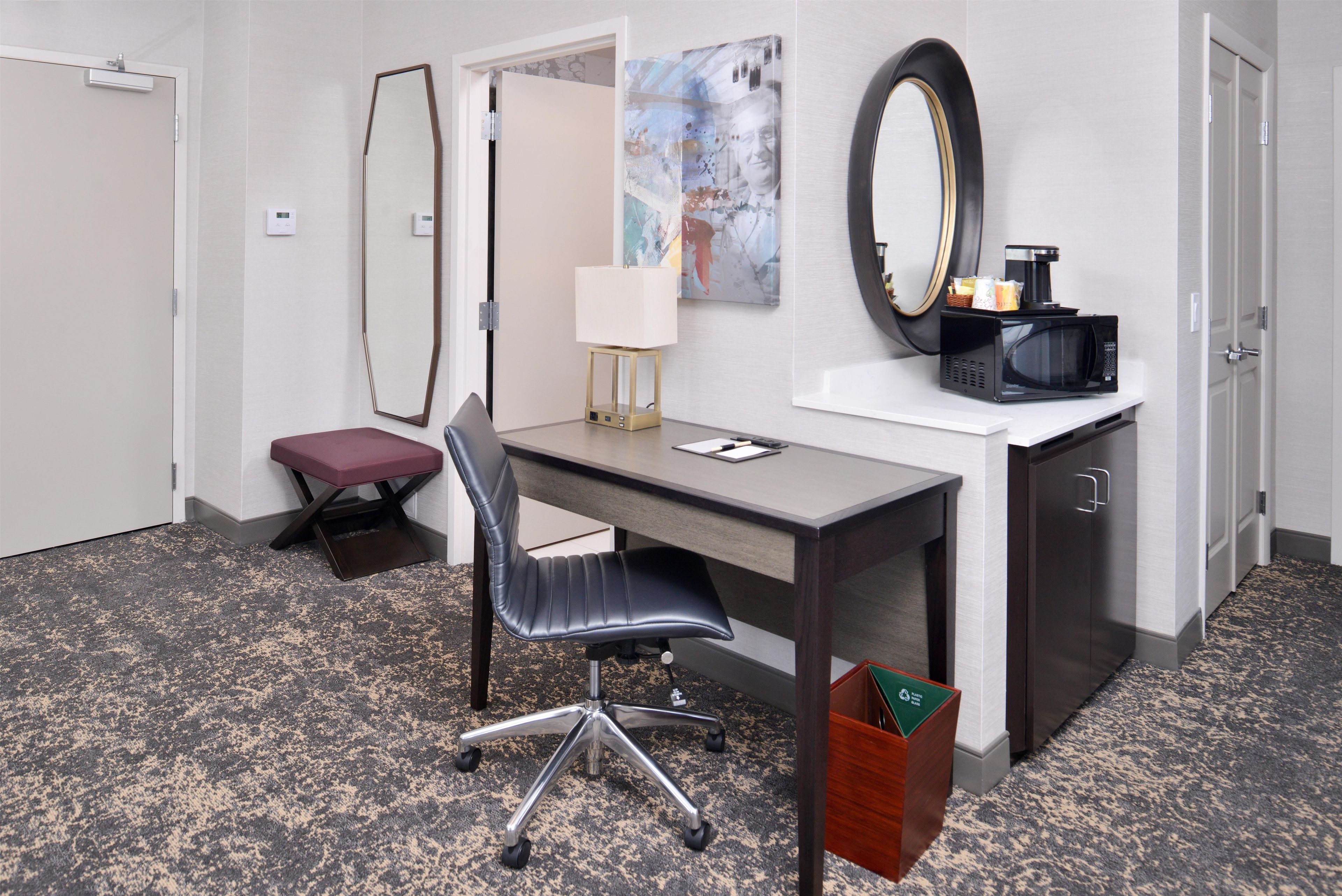 A hotel room with a desk, chair, and a microwave on a counter.