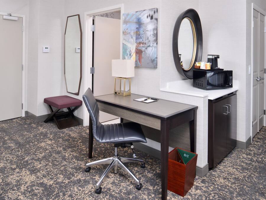 A hotel room with a desk, chair, and a microwave on a counter.
