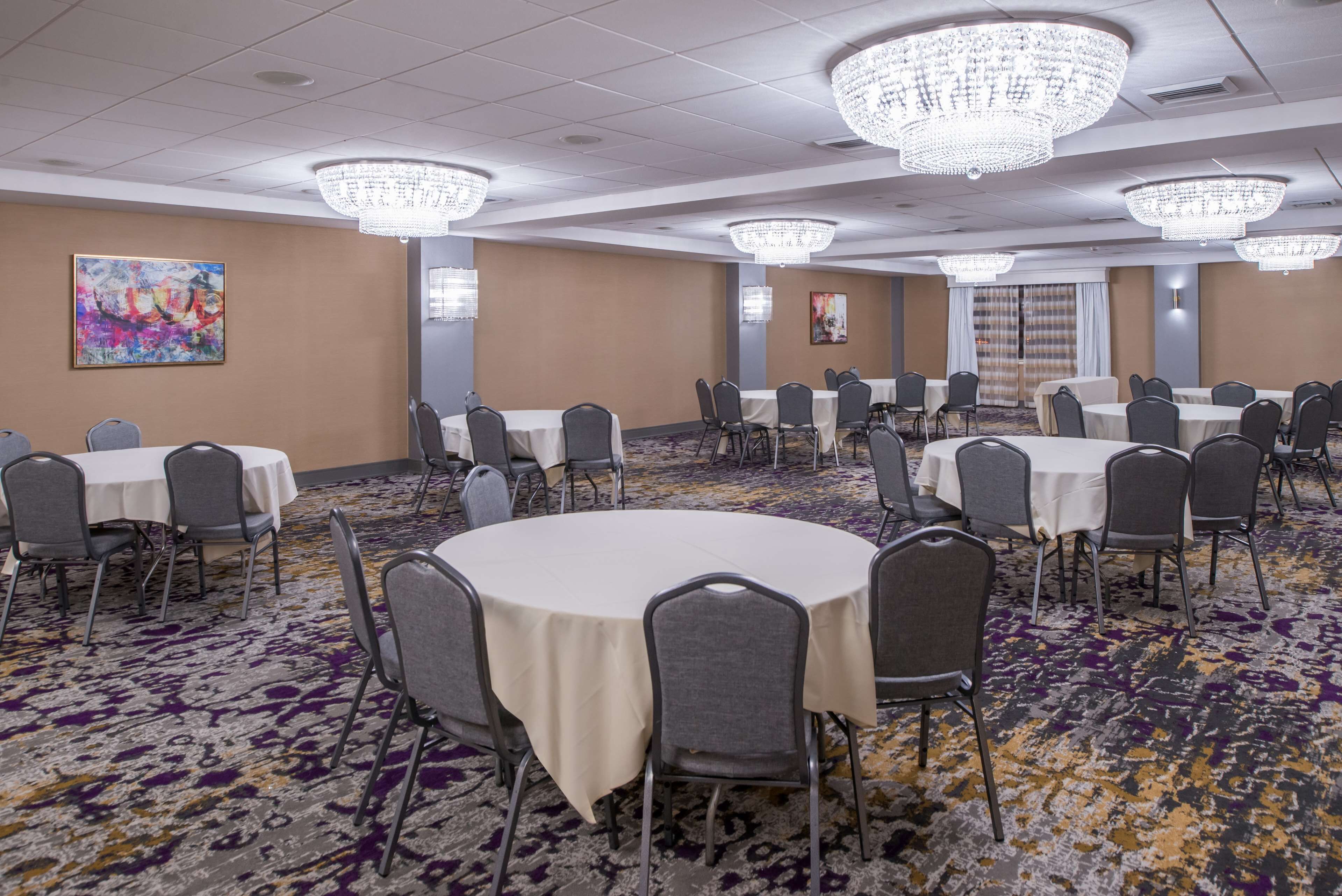 A conference room with round tables, gray chairs, and chandeliers.