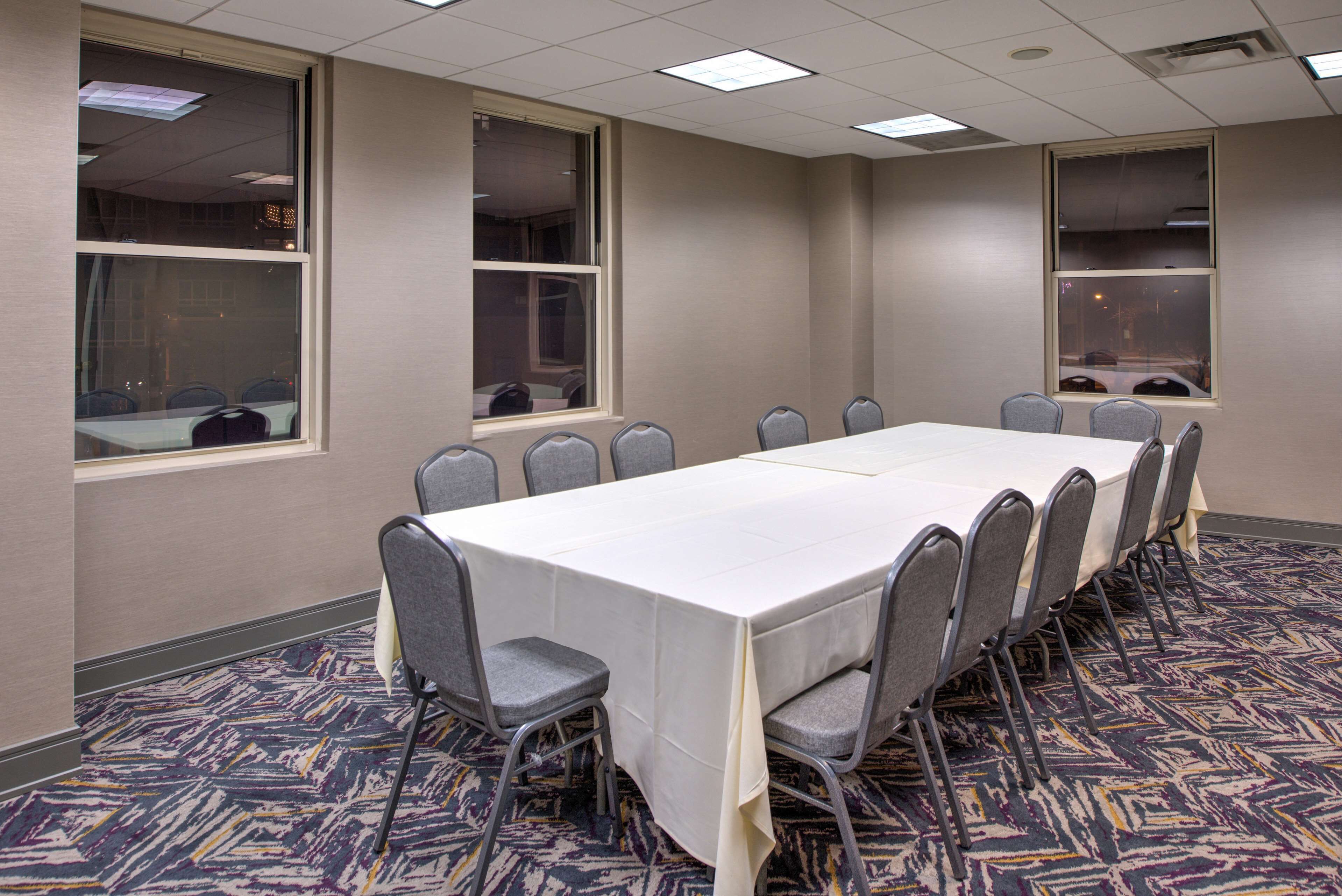 A conference room with a long table and chairs, large windows, and patterned carpet.
