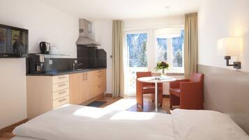 Habitación de hotel con cama, una pequeña mesa de comedor con sillas, una zona de cocina con cafetera y ventana con cortinas.