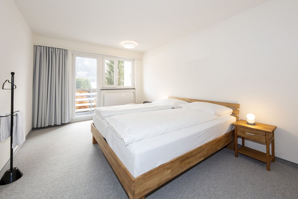 Un dormitorio con dos camas, una mesita de noche con lámpara, una lámpara de pie y un ventanal con cortinas.