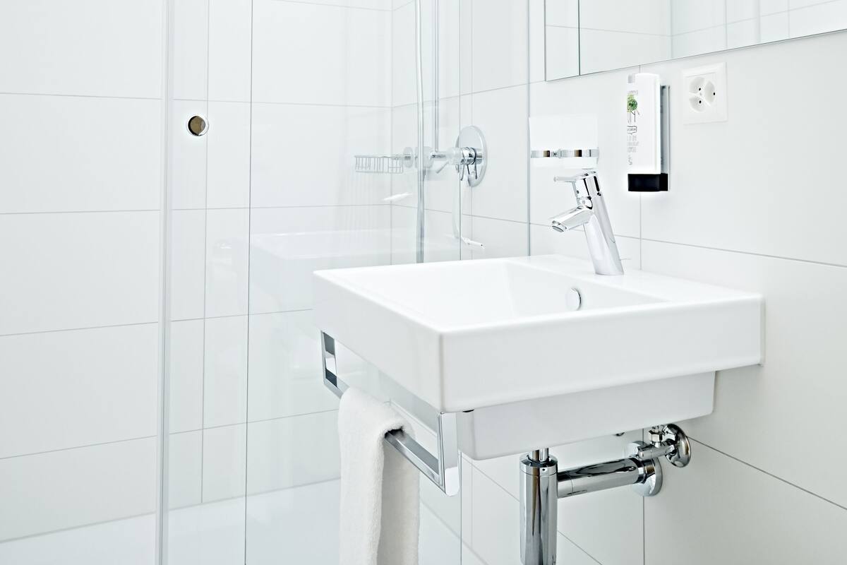 Un baño moderno con cabina de ducha de vidrio, un lavamanos blanco con una toalla y un espejo sobre él.