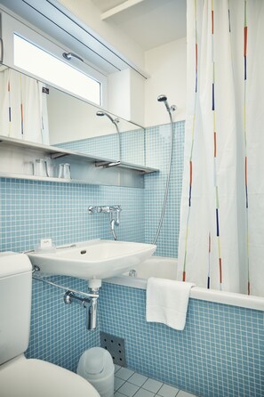 Un baño con un lavamanos blanco, un inodoro, una ducha con cortina de colores y un espejo sobre el lavamanos.