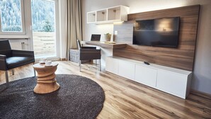 Una sala de estar moderna con un televisor grande, piso de madera, una mesa de centro redonda y vistas a un paisaje nevado a través de las ventanas.