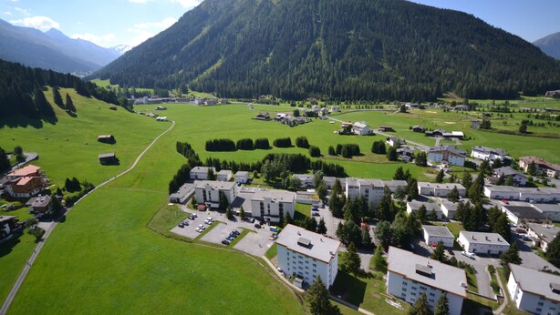 Zona residencial con varios edificios de apartamentos, campos verdes y una montaña al fondo.