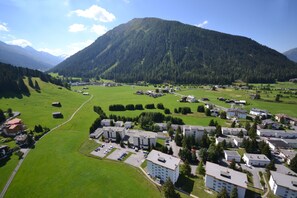 A residential area with multiple apartment buildings, green fields, and a mountain in the background. - Serviced Apartments by Solaria (Davos)
