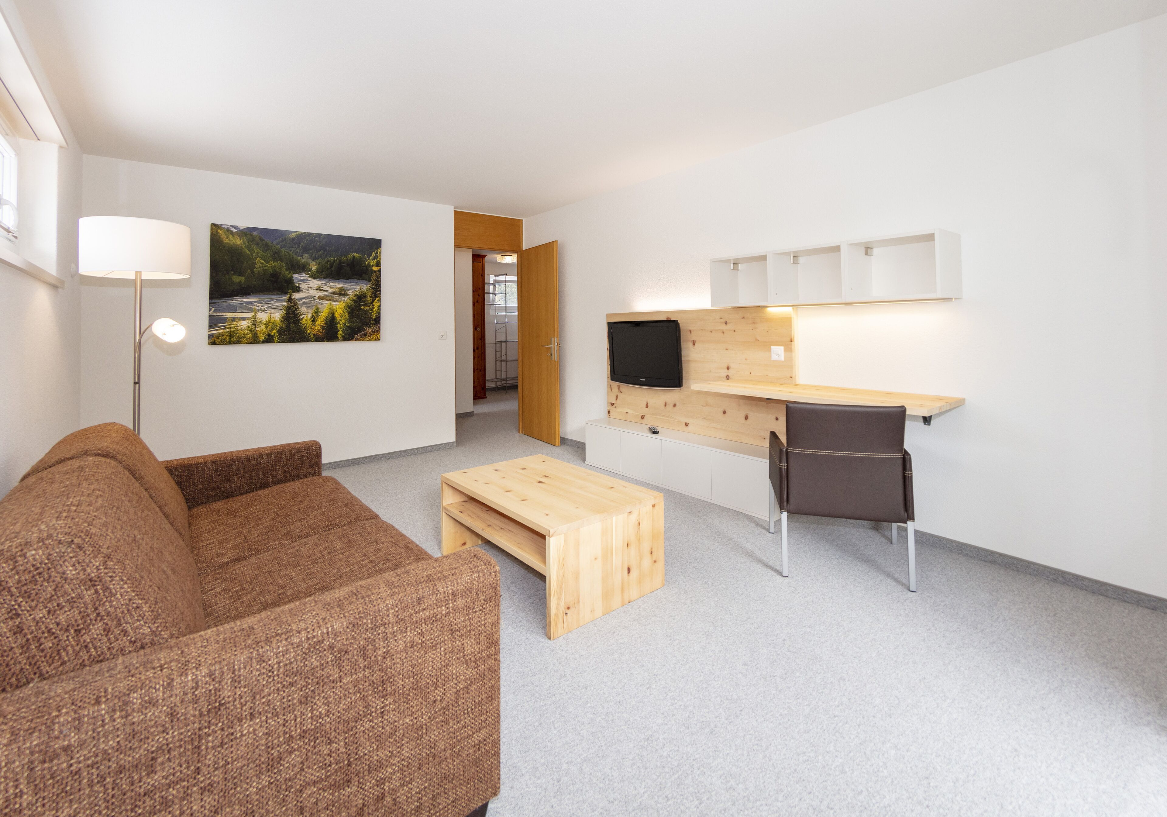 Un salon moderne avec un canapé marron, une table basse en bois, un téléviseur fixé à un mur en bois et un bureau avec une chaise.