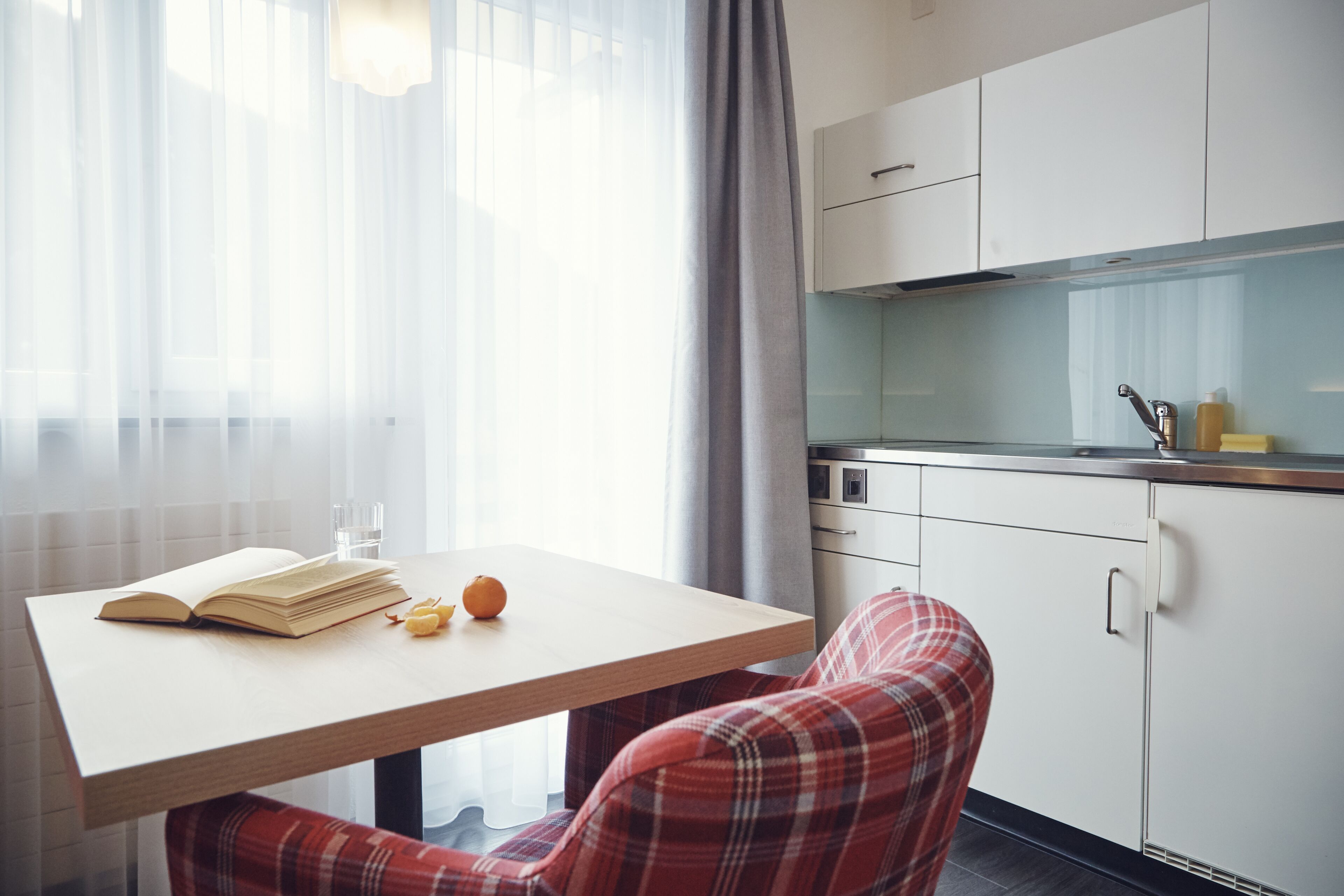 A modern kitchen with white cabinets, a wooden countertop, and a window with sheer curtains.