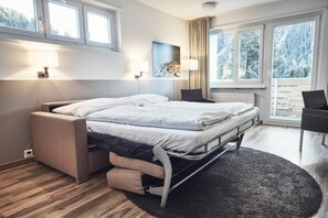 Habitación de hotel moderna con una cama, mesitas de noche, un escritorio y vistas a un bosque nevado a través de amplios ventanales.
