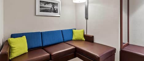 Un sofá modular marrón con cojines azules y amarillos, una fotografía en blanco y negro enmarcada en la pared y una lámpara de pie.