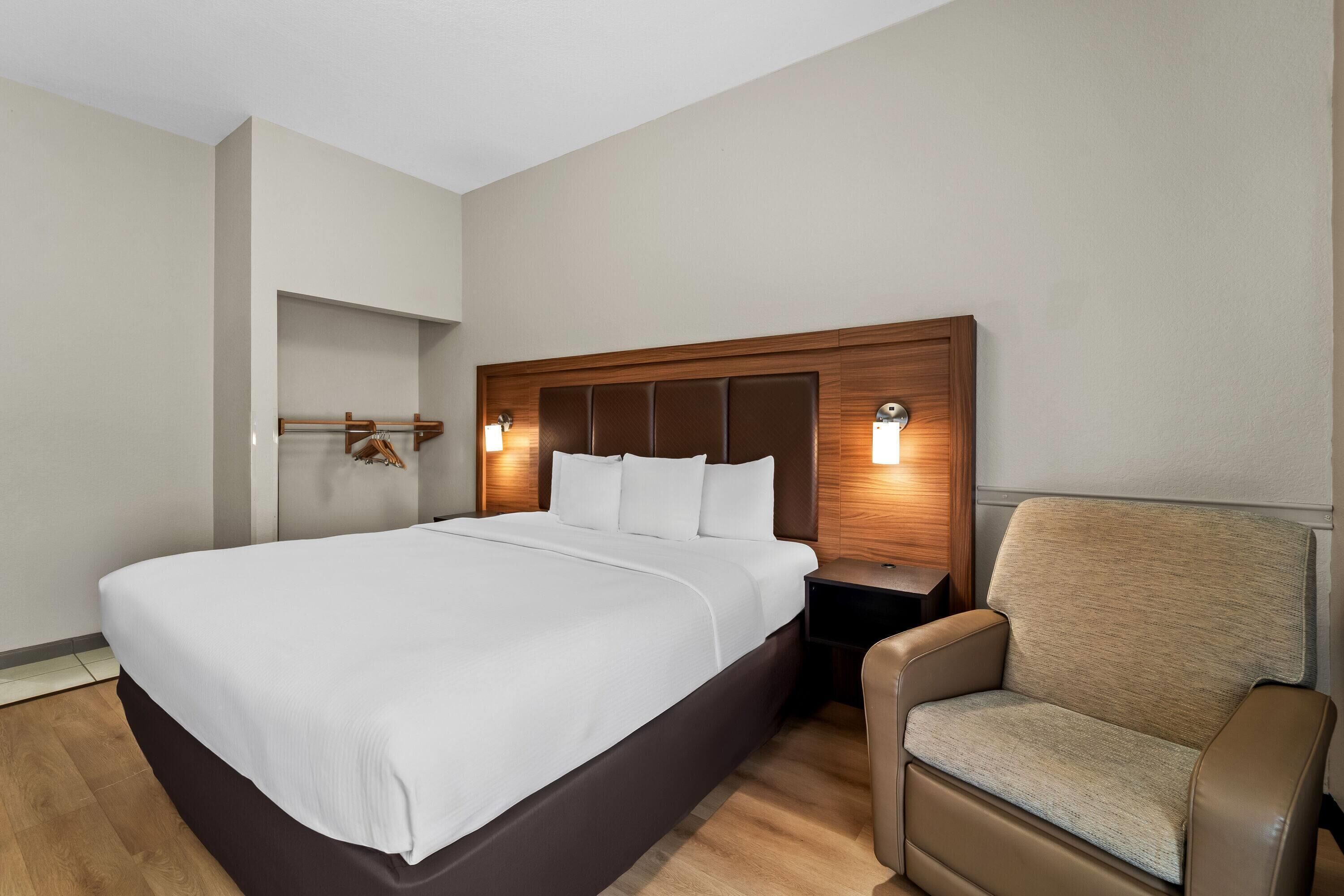 A hotel room with a large bed, a wooden headboard, a nightstand, and a chair.
