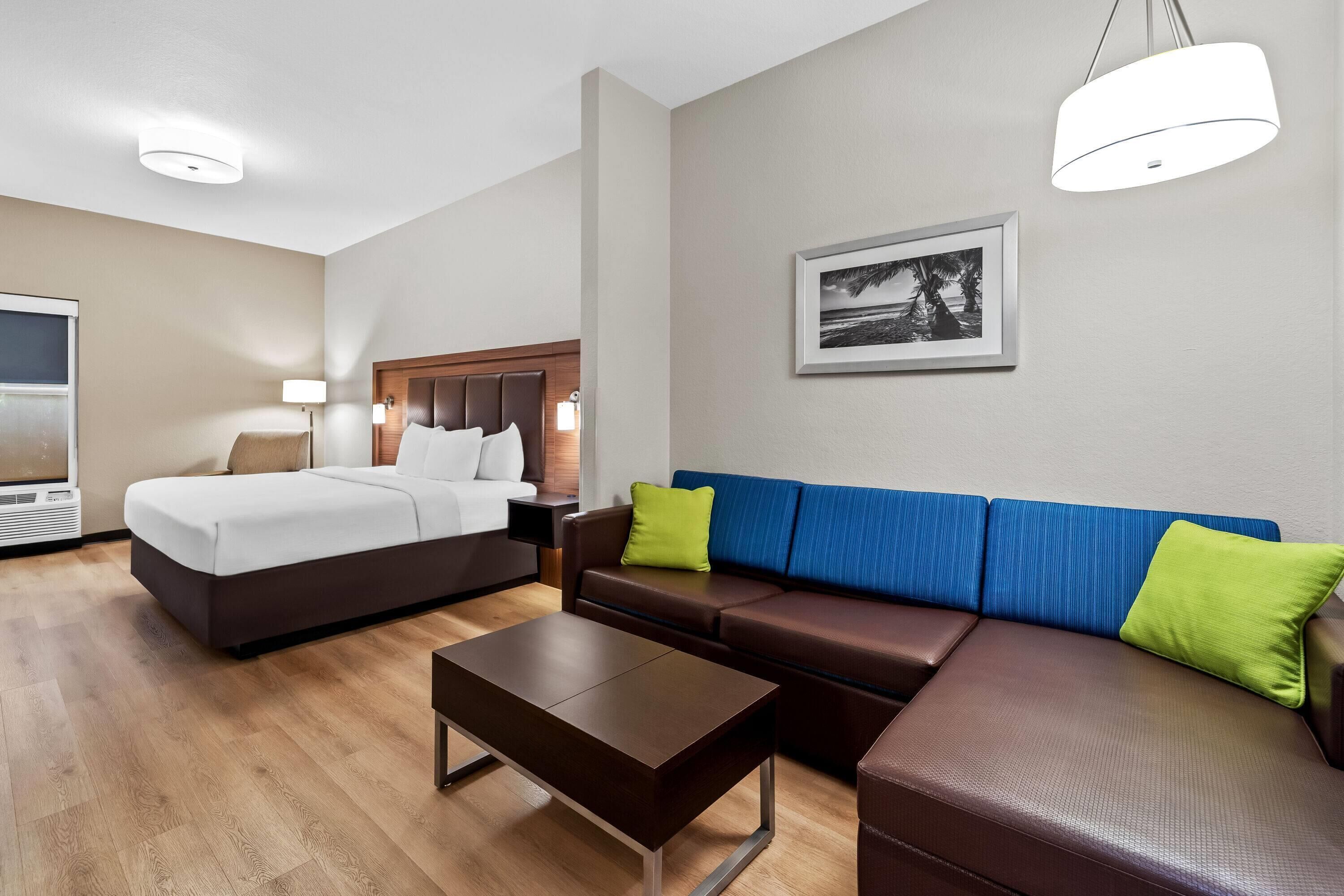 A hotel room with a bed, a sofa, a coffee table, a TV, and a wall-mounted picture.