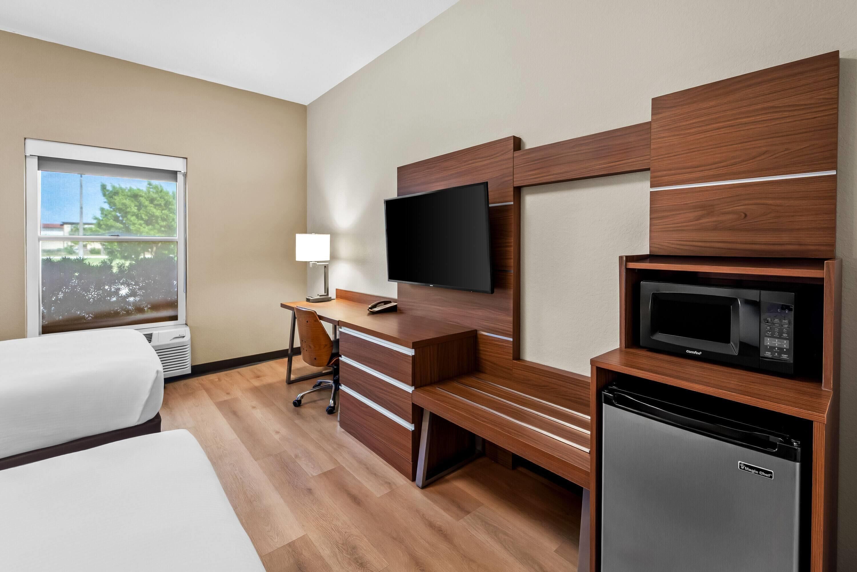 Habitación de hotel con cama, escritorio con computadora, televisión, microondas y refrigerador.