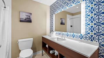 A bathroom with a white toilet, a wooden vanity with a white sink, and a large mirror.
