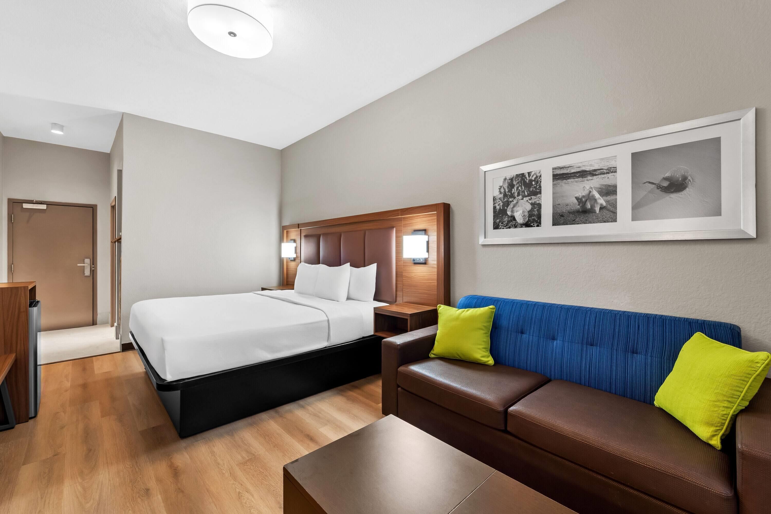 Una habitación de hotel con cama, sofá, mesita de café y un cuadro colgado en la pared.